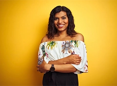 A person in a chic off-shoulder floral top and black pants, posing against a vibrant yellow backdrop.